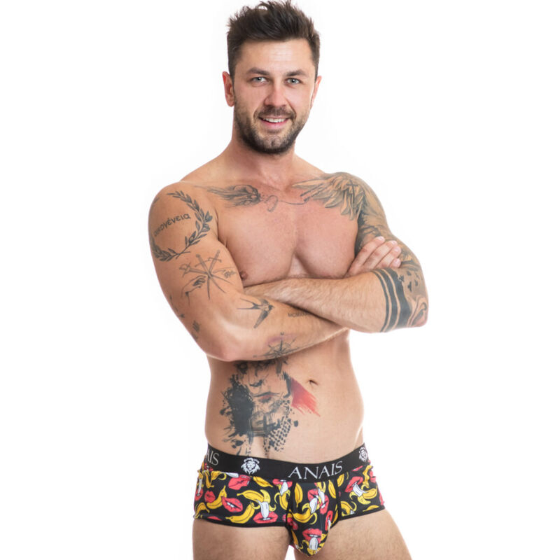 Muscular man standing with arms crossed, wearing colorful patterned boxer briefs and visible tattoos on chest and arms.