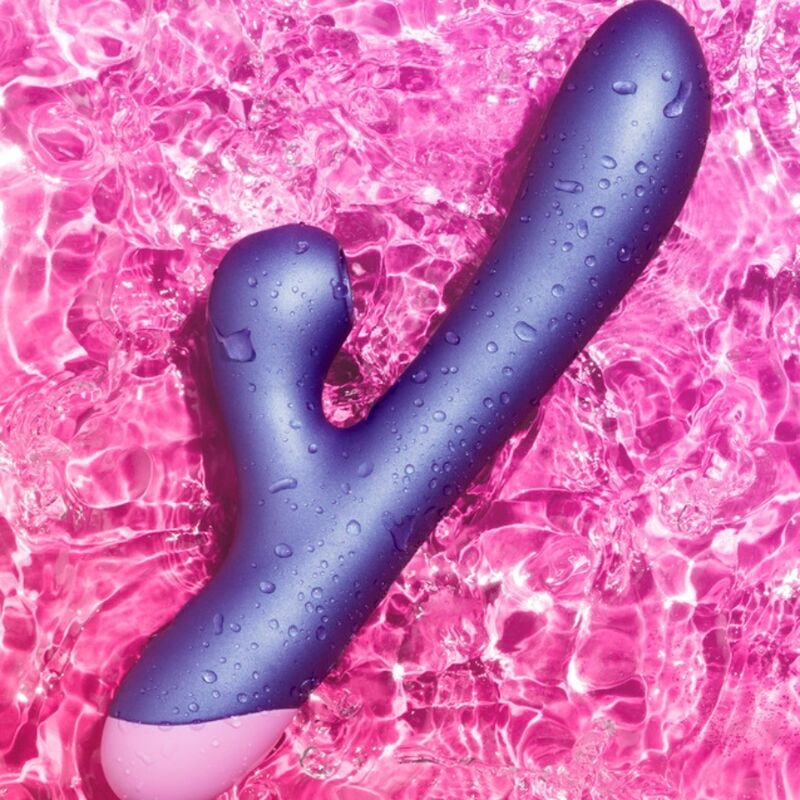 Curved purple vibrator with a pink base lying on pink water ripples. (Sex toy product image)
