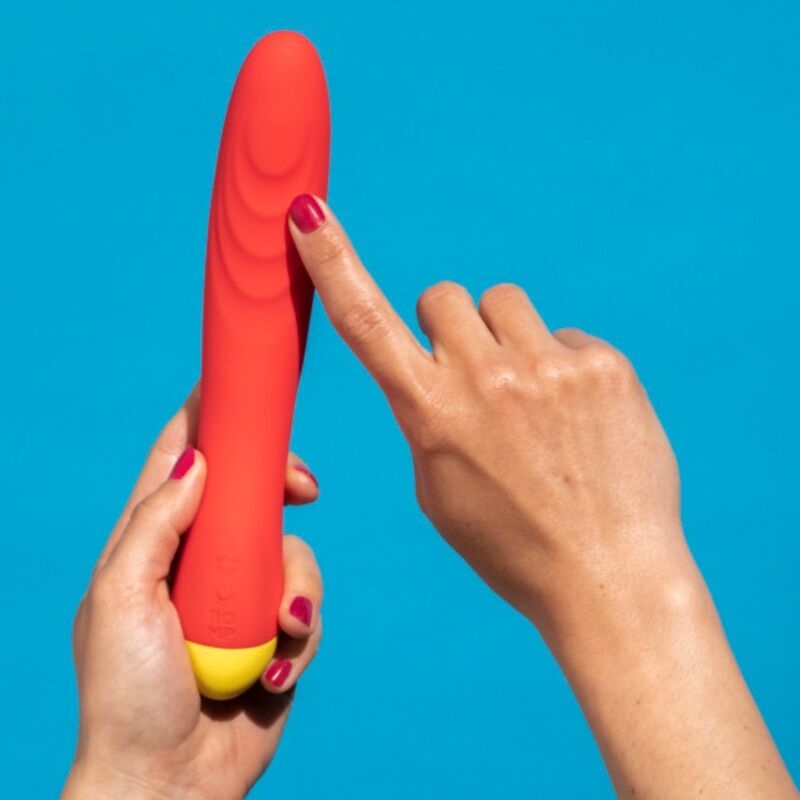 Red silicone vibrator with a yellow base held upright by a hand against a blue background.