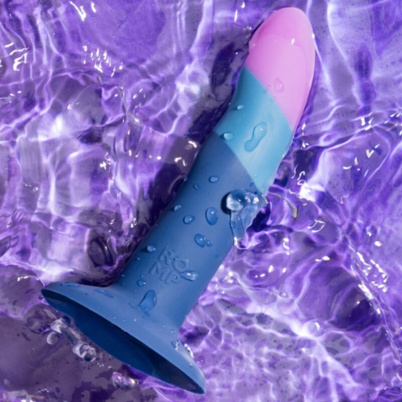 Blue and pink silicone sex toy submerged in purple water, droplets on the surface.