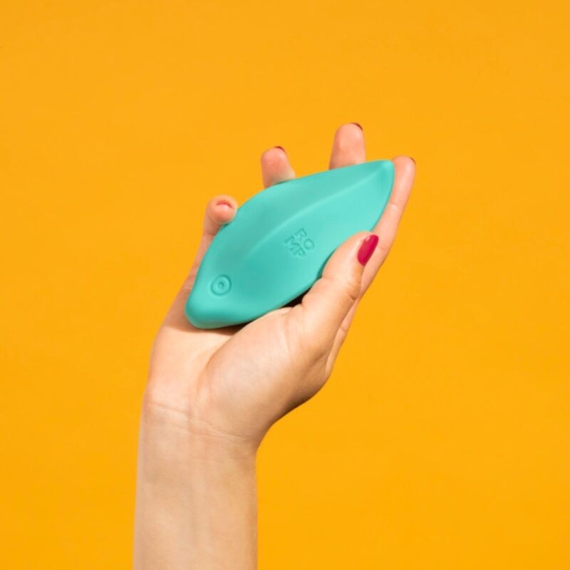 Hand holding a teal silicone personal massager with a power button against an orange background.