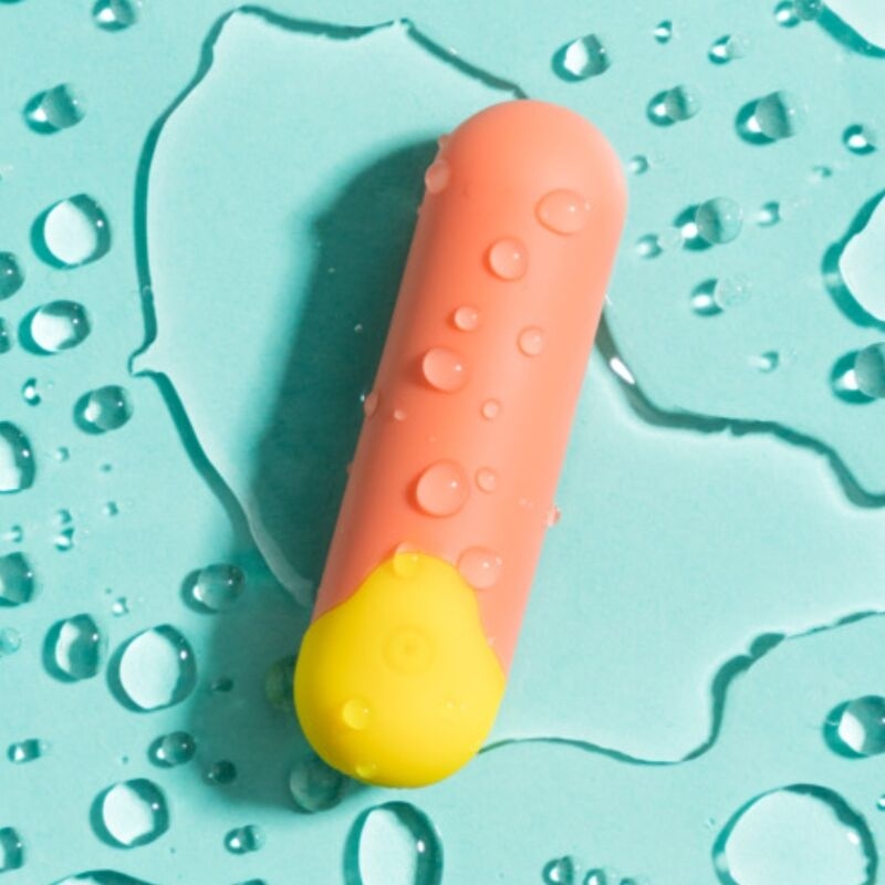Close-up of a pink silicone vibrator with a yellow base on a turquoise surface with water droplets nearby.