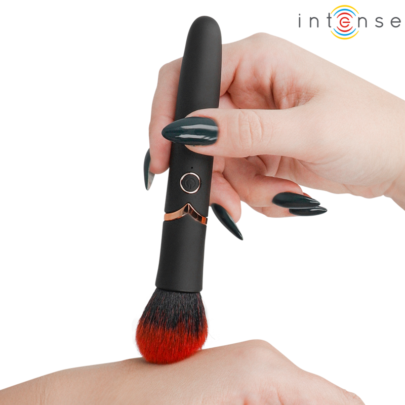 Hand with dark nail polish holds a black makeup brush against a forearm, showing makeup application; Intense logo top right.