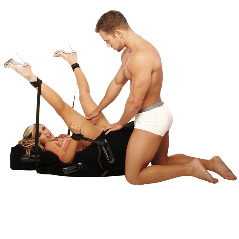 Couple using a sex chair with restraints: woman in lingerie strapped to the chair while a man kneels beside her.